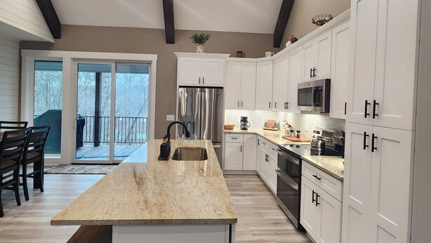 A modern kitchen with white cabinets, a large island, and a view to the outside. - Peaceful New Home Close to Helen/Hot Tub/Theater/Game Room/Firepit (Cleveland)