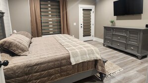 A bedroom with a bed, a ceiling fan, a TV, a dresser, and a door with a window. - Peaceful New Home Close to Helen/Hot Tub/Theater/Game Room/Firepit (Cleveland)