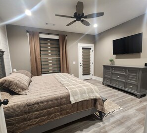A bedroom with a bed, a ceiling fan, a TV, a dresser, and a door with a window. - Peaceful New Home Close to Helen/Hot Tub/Theater/Game Room/Firepit (Cleveland)