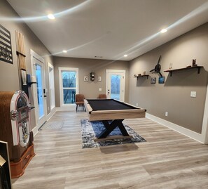 Una habitación amplia con mesa de billar, portaobjetos para billar y puerta que da a un balcón.