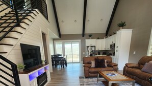A spacious living area with a modern kitchen, a fireplace, and a dining area with a view to the outdoors. - Peaceful New Home Close to Helen/Hot Tub/Theater/Game Room/Firepit (Cleveland)