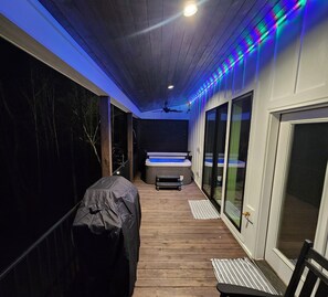 Una terraza techada al aire libre con jacuzzi, piso de madera y ventilador de techo.