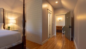A bedroom with a four-poster bed, a bedside lamp, and a wooden floor.
