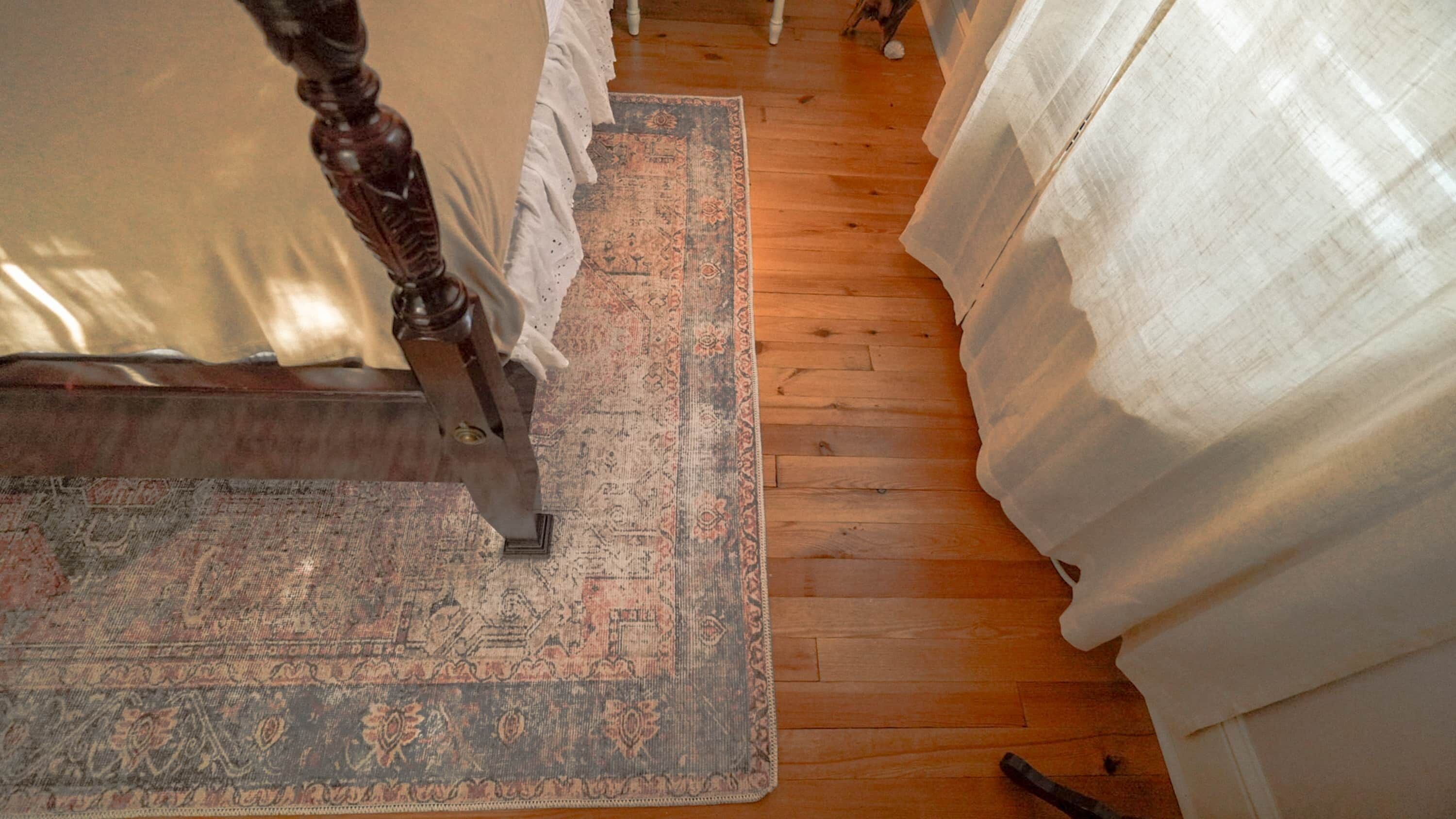 A room with a wooden floor, a patterned rug, and white curtains.