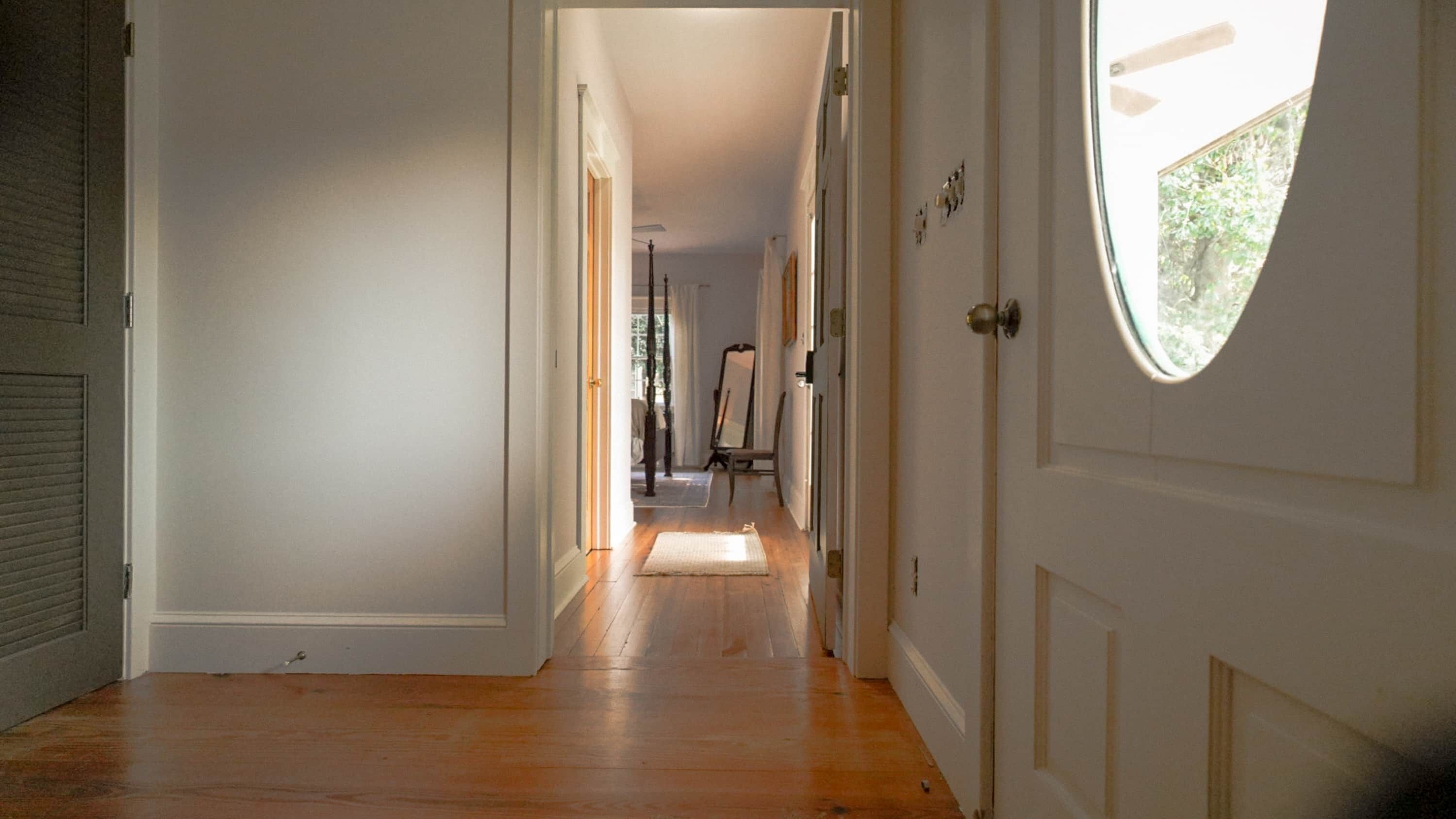 A hallway with wooden flooring, white walls, and a door with a window.