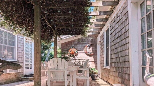 Une terrasse en bois agrémentée d’une pergola, de chaises Adirondack blanches et d’une table.