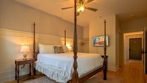 Un lit à baldaquin avec un ventilateur de plafond, une table de chevet avec une lampe, un téléviseur fixé au mur et un tapis à motifs.