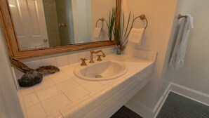 Ein Badezimmer mit einem weißen Waschbecken, goldenen Wasserhähnen, einem großen Spiegel und einem Handtuchhalter.