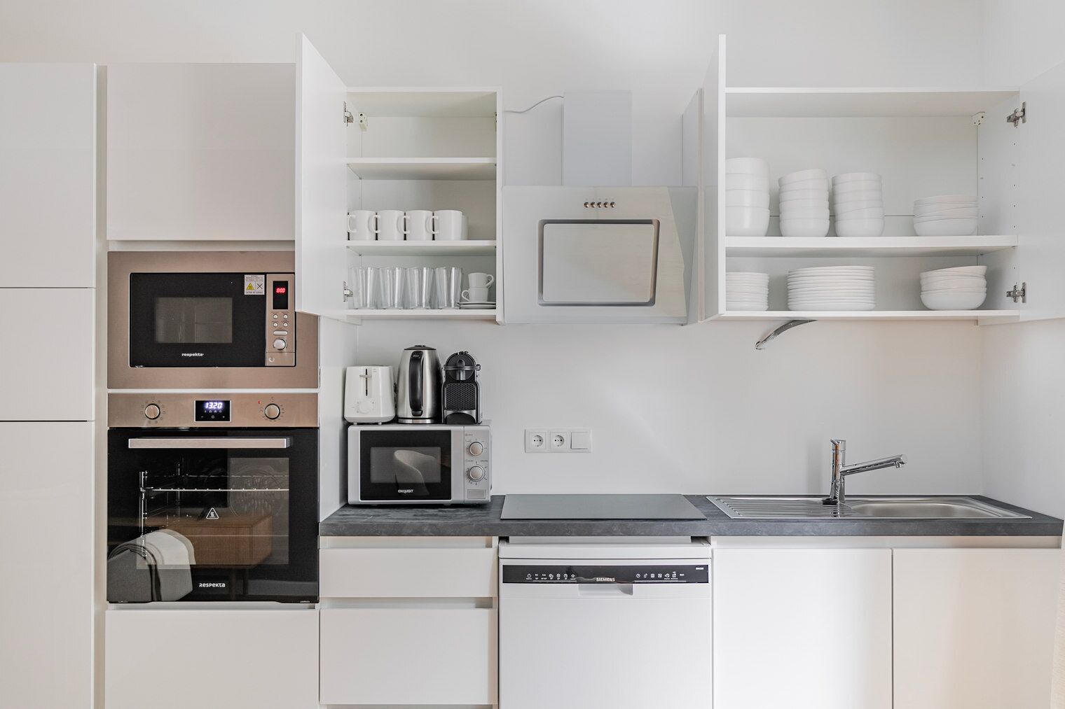 A modern kitchen with built-in appliances, including a microwave, oven, and dishwasher, and white cabinetry.