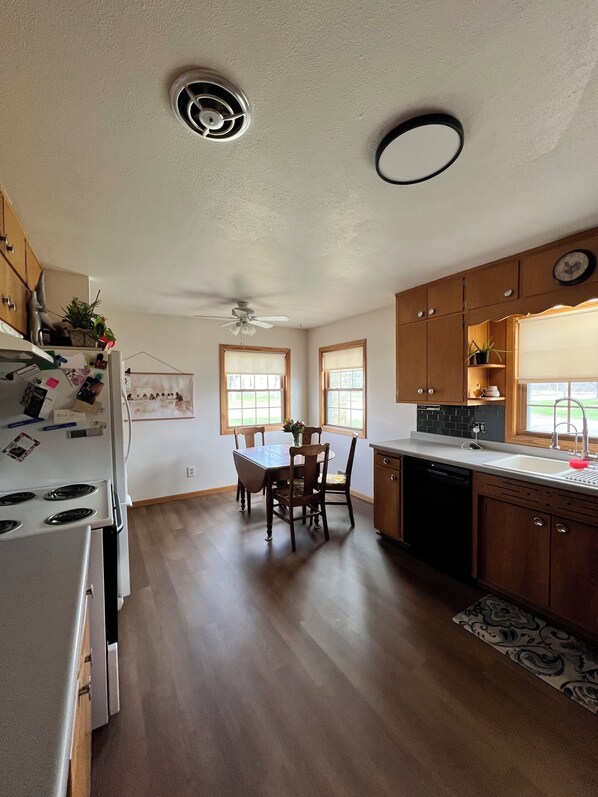 A kitchen with wooden cabinets, a white refrigerator, a dining table with chairs, and a ceiling fan.