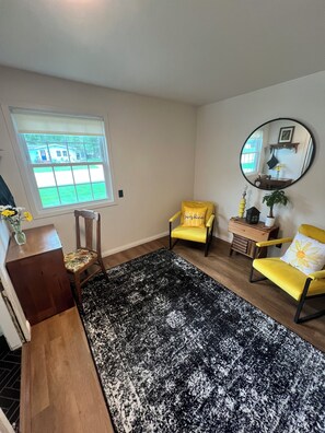 Um quarto com uma janela grande, duas cadeiras amarelas, um espelho redondo e um tapete preto e branco.