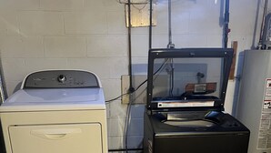 A laundry room with a white washer and dryer, a black appliance, and a small trash bin. - Guest Room on Mineral (Owatonna)