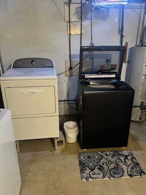 A laundry room with a white washer and dryer, a black appliance, and a small trash bin.