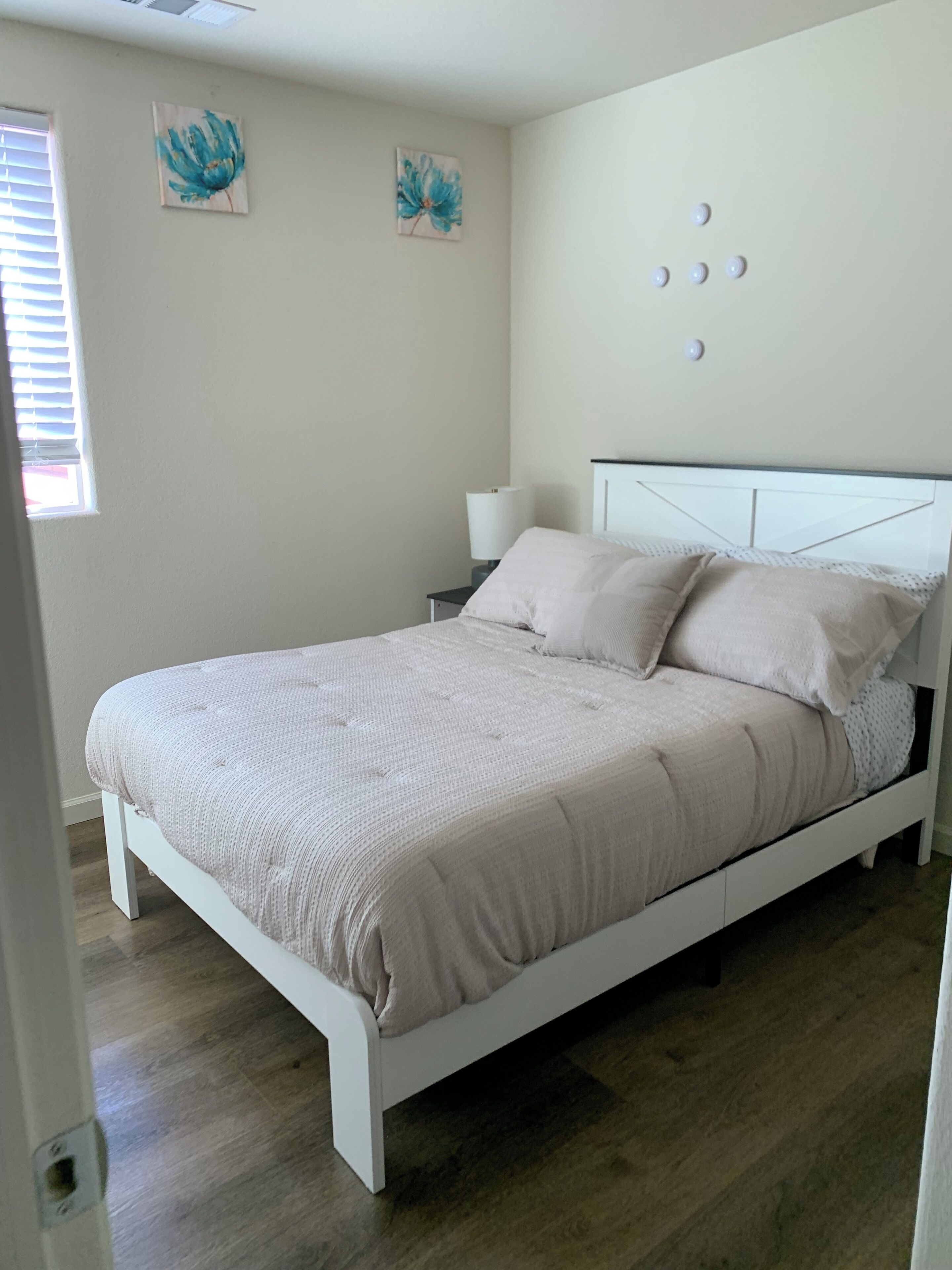 Un dormitorio con una cama blanca, una mesita de noche, una lámpara y dos luces fijadas a la pared.
