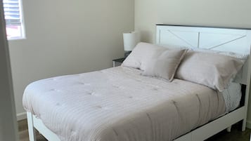 Un dormitorio con una cama blanca, una mesita de noche, una lámpara y dos luces fijadas a la pared.
