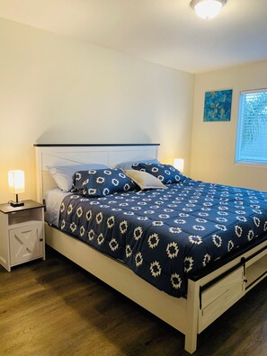 Una cama bien hecha con una colcha estampada, una mesita de noche con una lámpara y una ventana con persianas.