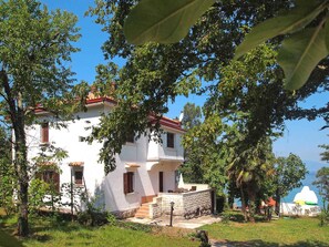 A white building with a red roof, surrounded by trees and a clear blue sky. - Holiday apartment Apartment Azzurra, first row to the sea (Njivice)