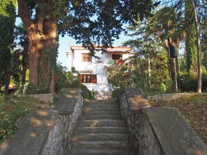 Eine Steintreppe führt zu einem weißen Gebäude mit rotem Dach, umgeben von Bäumen und Grünpflanzen.