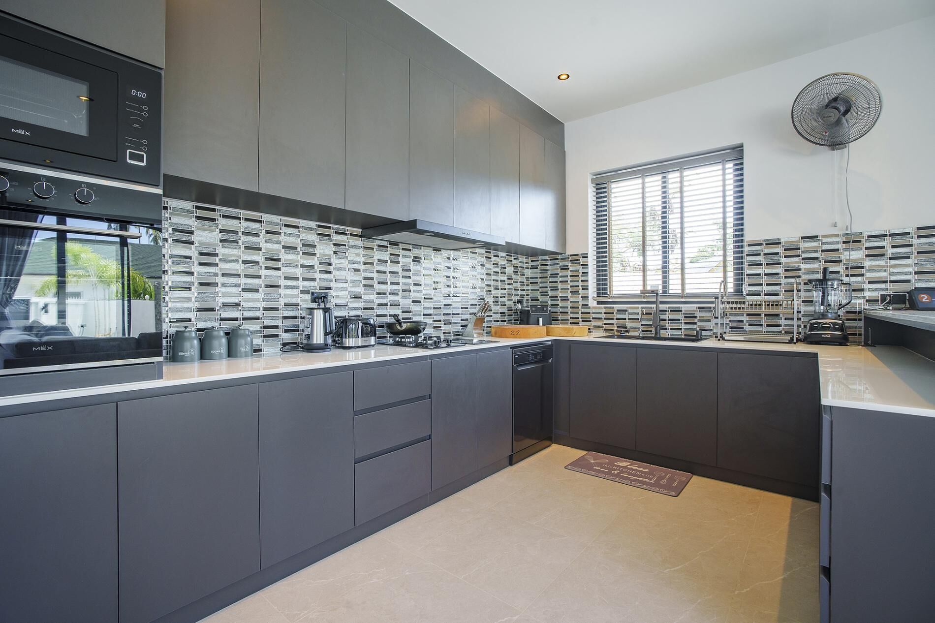 A modern kitchen with grey cabinetry, a large island, and a tiled backsplash.