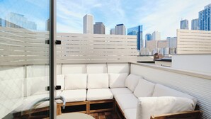 Una terrazza sul tetto con una zona relax in bianco imbottita, un tavolo in legno e vista sullo skyline della città.