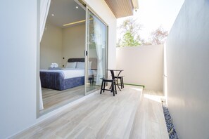 A modern bedroom with a large bed, a glass door leading to a balcony, and a small table with chairs. - New Celine Villa Private Pool Near Beaches (Rawai)