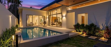 Una casa moderna con piscina, amplios ventanales y un área exterior bien iluminada.