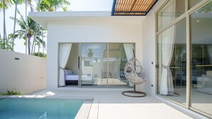 Un espace piscine extérieur moderne, doté d’une chambre à coucher entourée de baies vitrées, d’un fauteuil suspendu et offrant une vue sur les palmiers.