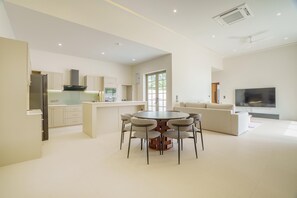 A modern kitchen with a central island, a dining area with four chairs, a sofa, and a TV in a living area. - New Celine Villa Private Pool Near Beaches (Rawai)