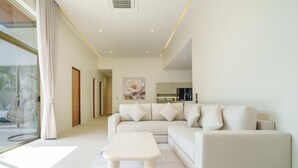Un salon moderne avec un canapé et une table basse, une cuisine à l’arrière-plan et une grande fenêtre avec des rideaux.