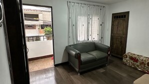 Un salon avec un canapé vert foncé, un pouf à motifs et une porte en bois.