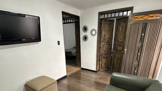 Un salon avec un canapé en cuir vert, un pouf beige et un téléviseur à écran plat fixé au mur.