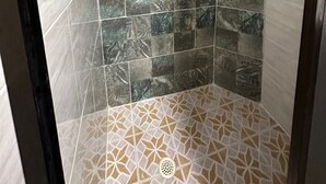 Une douche avec un carrelage au motif géométrique sur le sol et un mélange de motifs naturels et abstraits sur les murs.