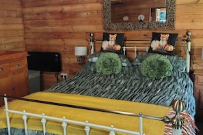 Ein Holzblockhaus-Interieur mit einem Bett, Kissen, einer Lampe, einem Spiegel und einem Fernseher.