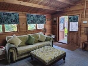 A wooden cabin interior with a sofa, ottoman, and curtains.