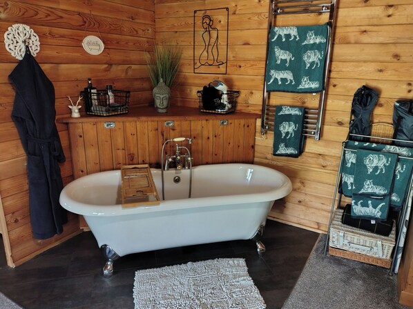 A bathroom with a freestanding bathtub, wooden walls, a towel rack with tiger-patterned towels, a small shelf with toiletries, and a decorative Buddha head.