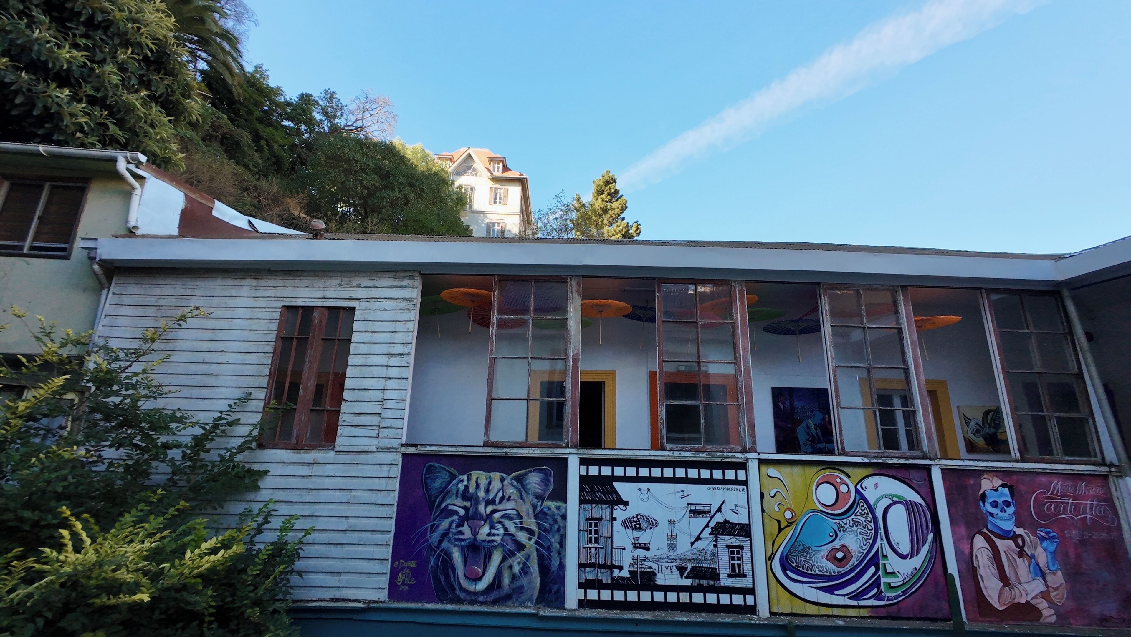 A building with large windows, a balcony with colorful murals, and a view of a hill.