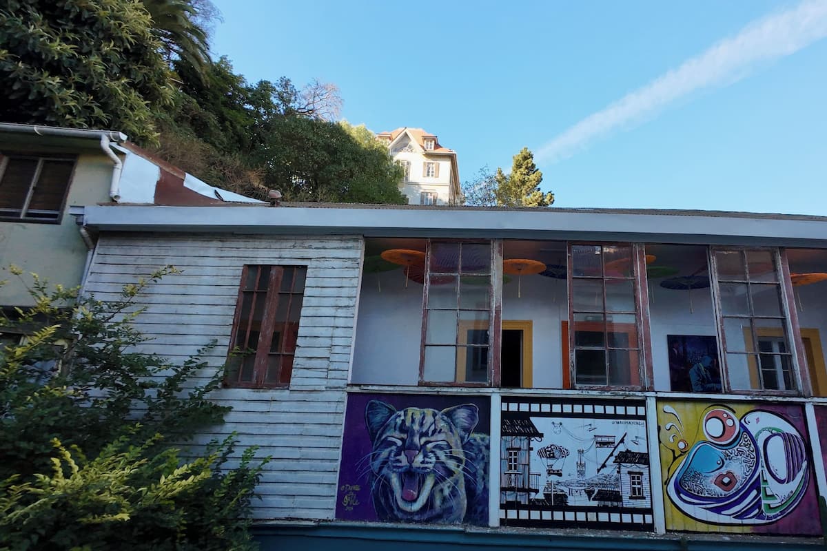 Un immeuble doté de grandes fenêtres, d’un balcon orné de peintures murales colorées et offrant une vue sur une colline.