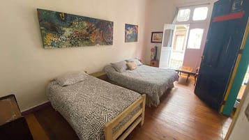A room with two beds, wooden flooring, and a door leading to an outdoor area.