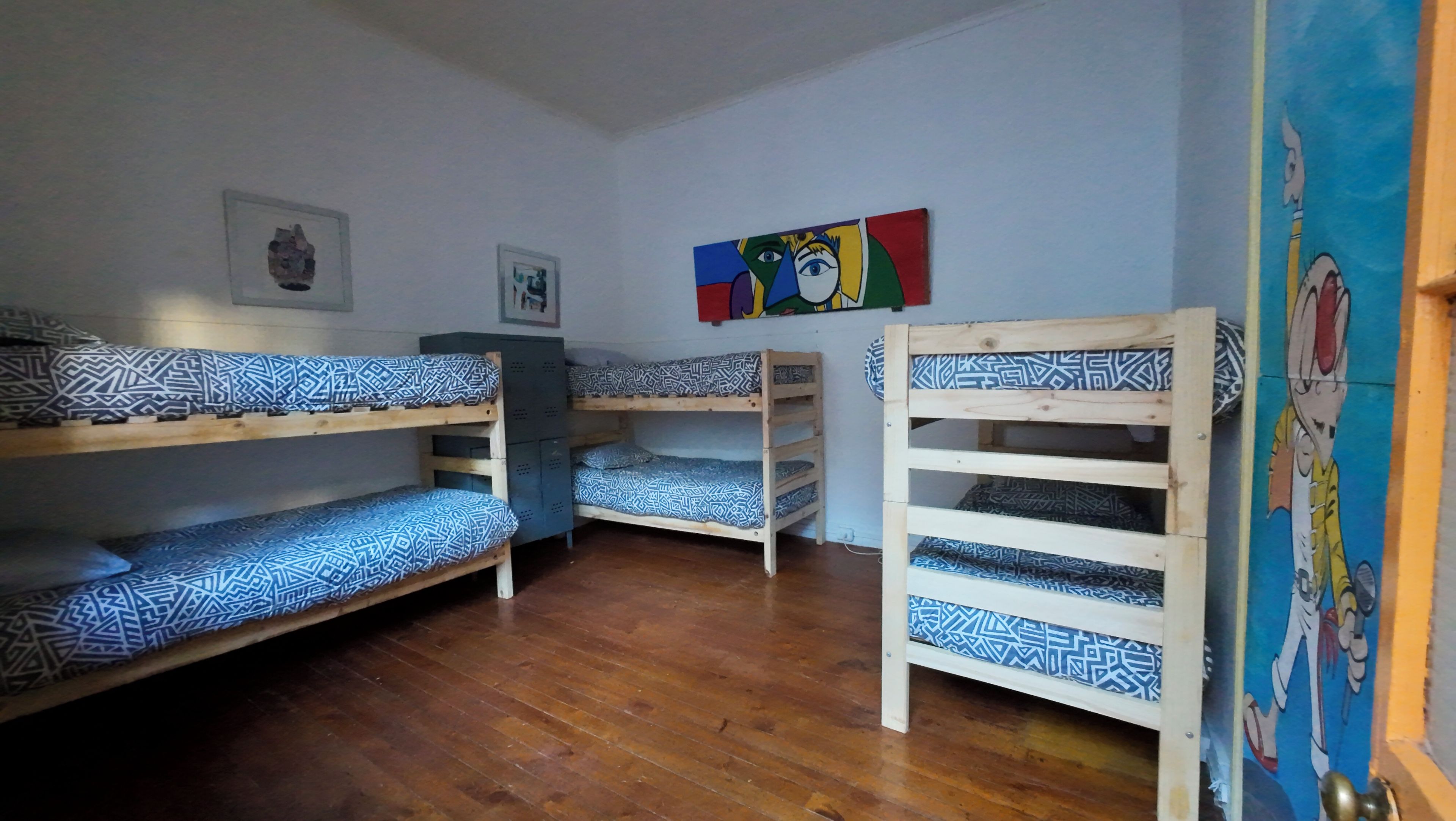 A bunk bed room with patterned bedding, a wooden floor, and a colorful painting on the wall.