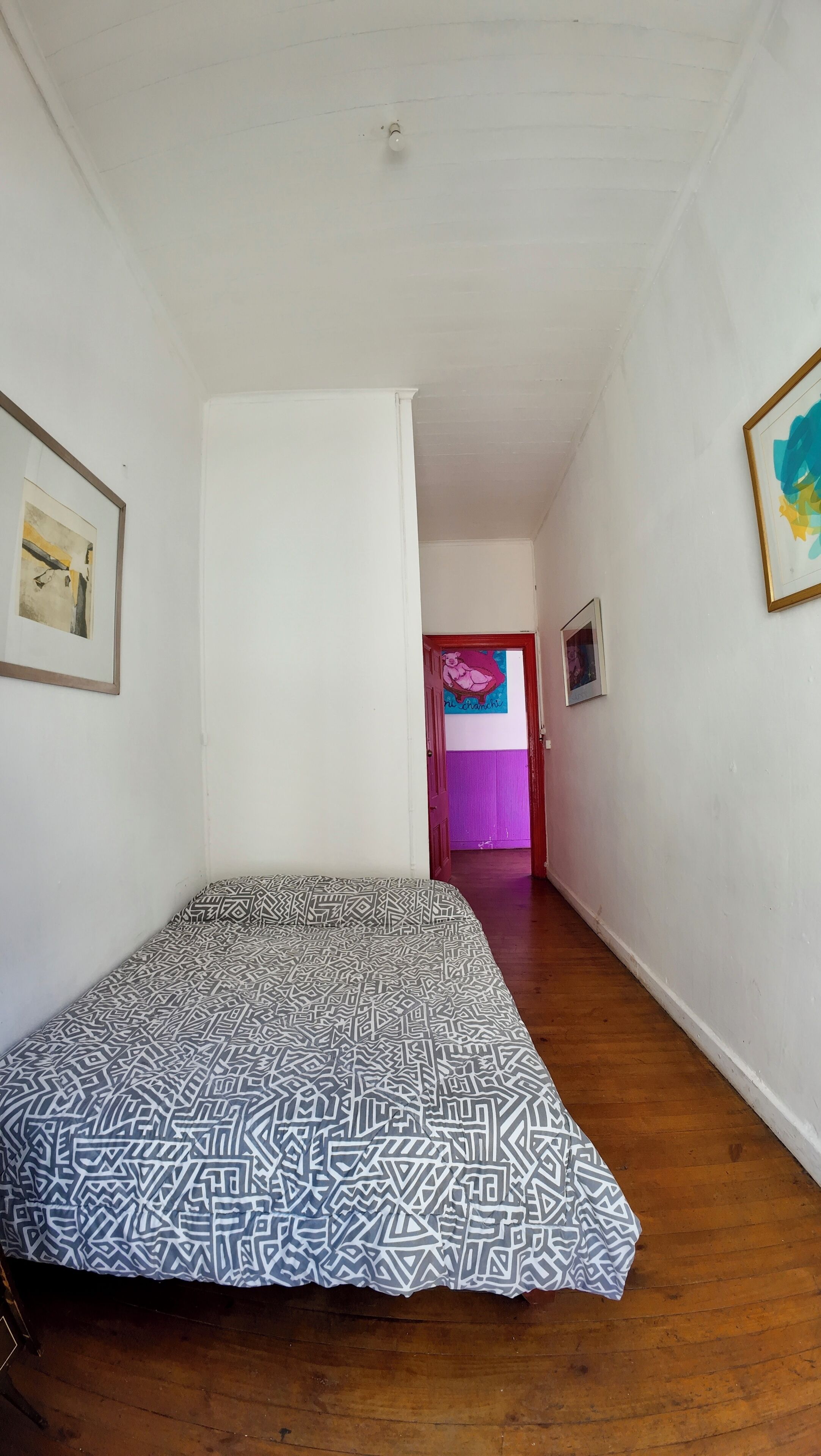 A room with a bed, a door leading to another room, and a framed picture on the wall.