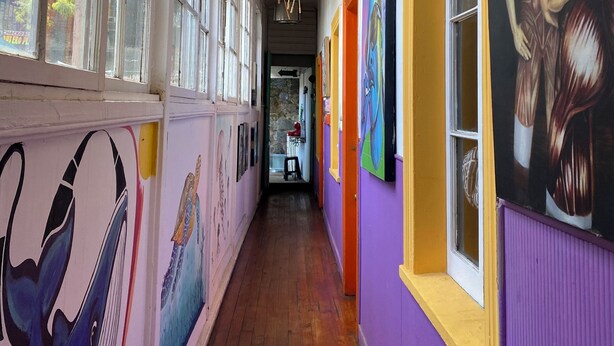 A hallway with colorful umbrellas hanging from the ceiling, large windows, and artwork on the walls. -  Hostal Valpito Cultura y Arte (Valparaíso)