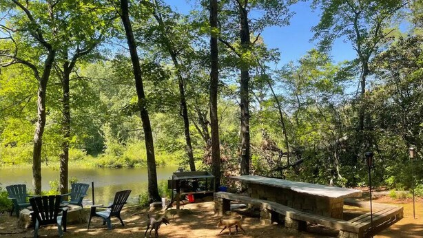 A lakeside campsite with Adirondack chairs, a picnic table, and a wooden deck.