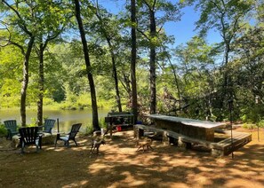 Un camping frente al lago con sillas Adirondack, una mesa de picnic y una terraza de madera.