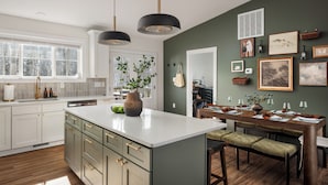 A modern kitchen with a large island, white cabinetry, and a dining area with a wooden table and chairs.