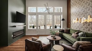 A modern living room with a green sofa, leather chairs, a fireplace, and a TV mounted on the wall.