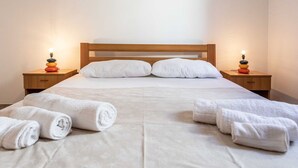 Ein ordentlich bezogenes Bett mit weißen Leinen und Kissen, zwei Nachttische mit Lampen und aufgerollte Handtücher auf dem Bett.