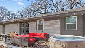 Een huis met een patio, voorzien van een rieten bank met rode kussens, een eettafel met stoelen en een hottub.