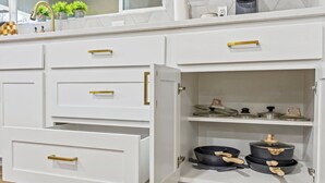 Een keuken met witte kastjes, gouden knoppen en een aanrecht met potplanten.