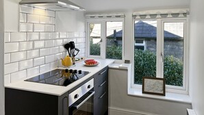 A modern kitchen with white tiles, a black stove, and a window with a view of greenery. - Ashridge, near Lynton (Lynton)