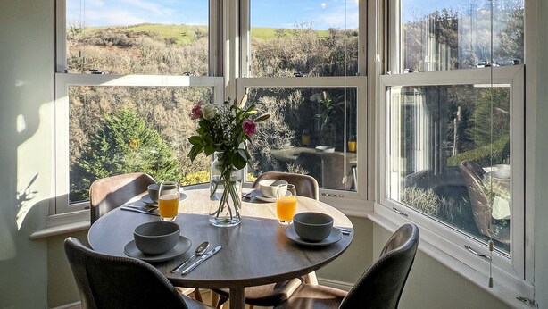 A dining area with a round table, chairs, and a view of a landscape through large windows. - Ashridge, near Lynton (Lynton)